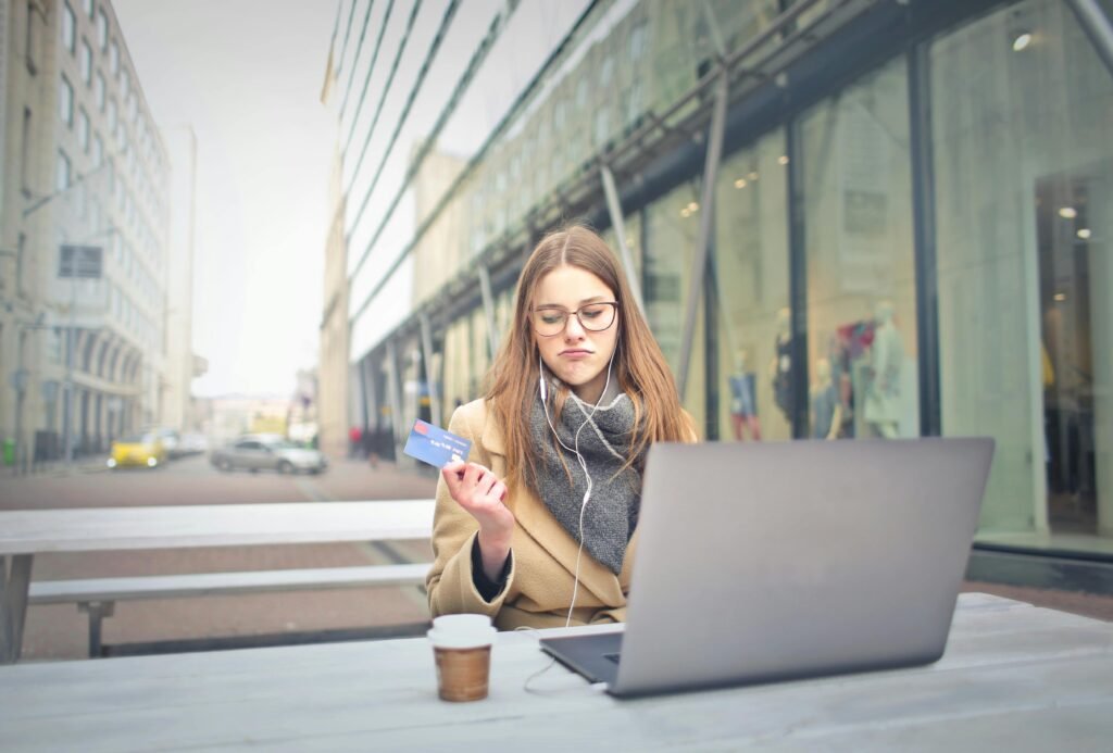 Young woman with credit card using laptop for online shopping outside in an urban setting.